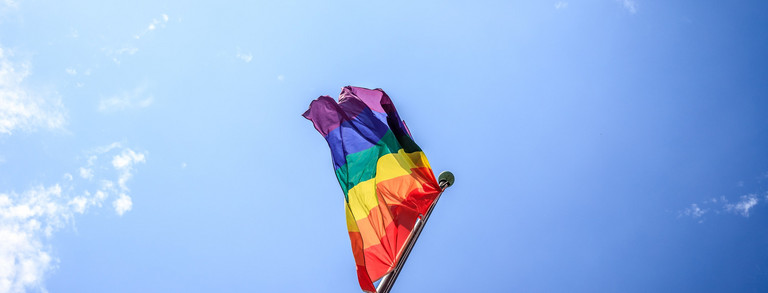 bunte Flagge, Regenbogenflatte vor blauem Wolkenhintergrund