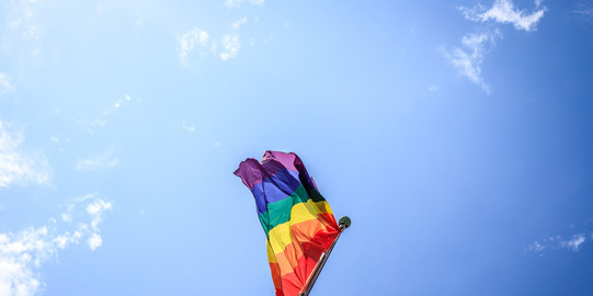 bunte Flagge, Regenbogenflatte vor blauem Wolkenhintergrund